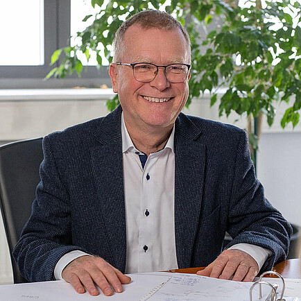 Drei Personen stehen zur Besprechung an einem Tisch.